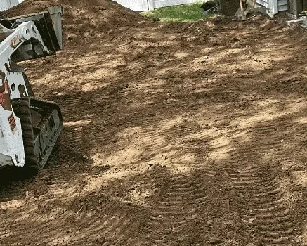 Skid steer grading the subgrade of a back yard before Baudi Landscaping laid a paver patio