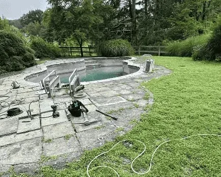 Cracked, moss-grown flagstone pool surround with the pool drained, before Baudi Landscaping rebuilt it