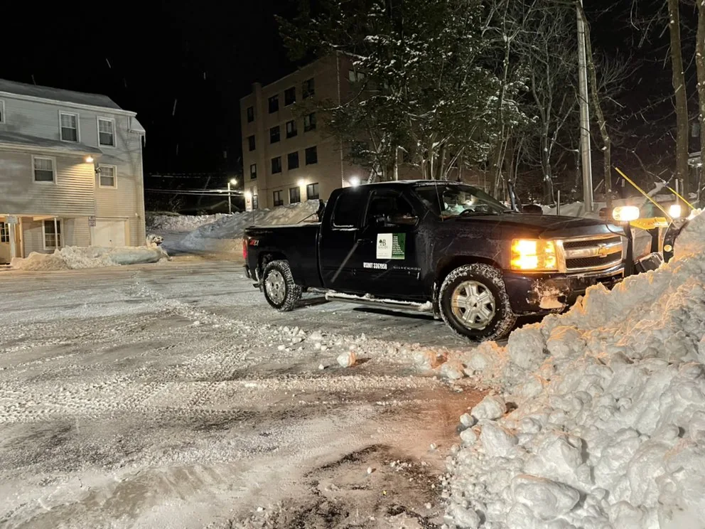 Baudi plow truck clearing a Westchester lot at night during a snowstorm