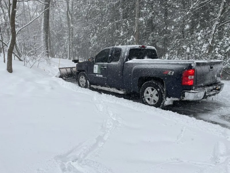 Baudi Landscaping pickup with the plow blade down, clearing a wooded Westchester driveway mid-storm
