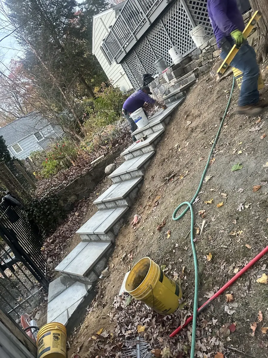 Baudi mason setting new stone treads on a slope, with stone veneer work underway behind him at a Westchester home