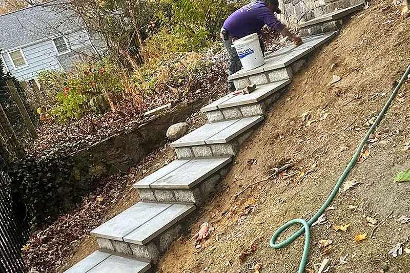 Baudi crew member setting a granite tread on a run of stone steps cut into a slope in Westchester County, NY